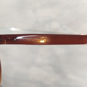 May include: Close-up of the brown plastic arm of a pair of glasses with the text "BAUSCH & LOMB" embossed on it.