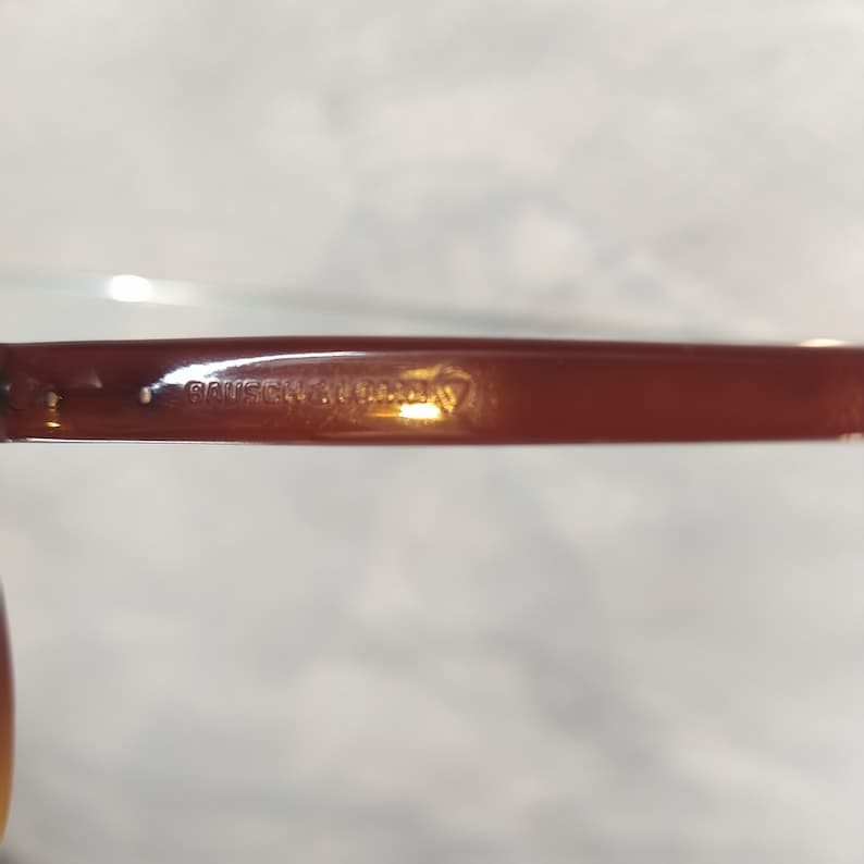 May include: Close-up of the brown plastic arm of a pair of glasses with the text "BAUSCH & LOMB" embossed on it.