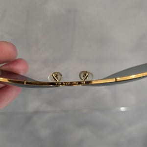 Puede incluir: Primer plano del interior de unas gafas de sol de montura dorada con el texto "Ray-Ban  USA" impreso en la montura.