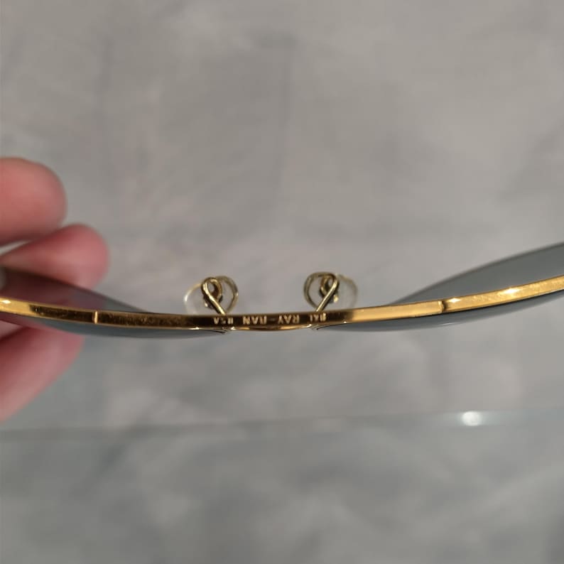 Puede incluir: Primer plano del interior de unas gafas de sol de montura dorada con el texto "Ray-Ban  USA" impreso en la montura.