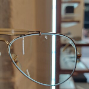 May include: Close-up of a gold-rimmed aviator sunglasses with a blue lens. The sunglasses have a small inscription on the lens that reads "RL".