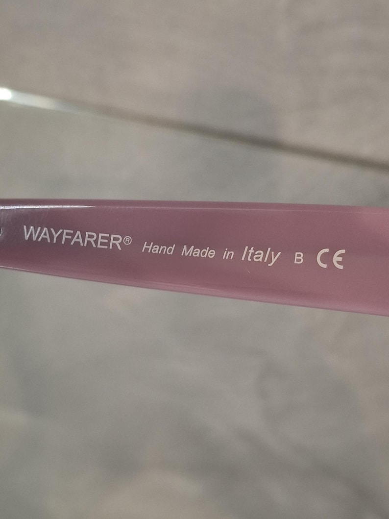 Puede incluir: Primer plano de una patilla de gafas Wayfarer rosa. El texto "WAYFARER&reg; Hand Made in Italy B CE" est&aacute; impreso en blanco en la patilla. La patilla es de color rosa claro liso.