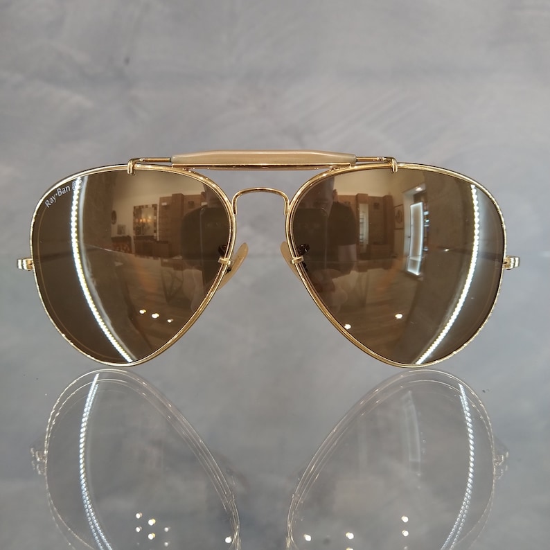 May include: Gold aviator sunglasses with brown mirrored lenses. The sunglasses have a Ray-Ban logo on the left lens.