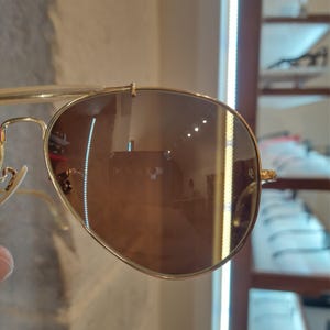 May include: Gold aviator sunglasses with brown lenses. The sunglasses are reflecting the interior of a store.