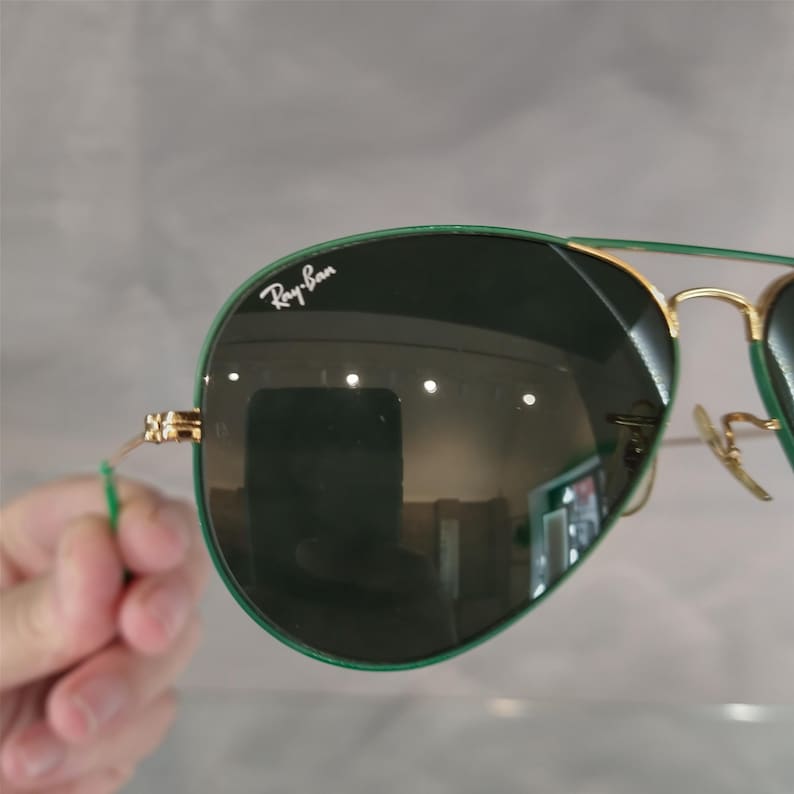 Op de afbeelding: Groene Ray-Ban aviator zonnebril met gouden montuur en donkergroene glazen. De zonnebril heeft het Ray-Ban logo op de linker lens.