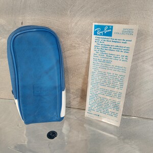 May include: A blue and white Ray-Ban sunglasses case with the Ray-Ban logo on the front. The case is made of a soft, durable material and is designed to protect your sunglasses from scratches and damage. The case is also lightweight and easy to carry.