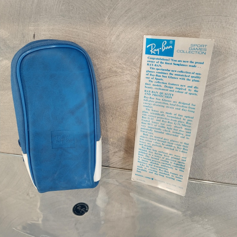 May include: A blue and white Ray-Ban sunglasses case with the Ray-Ban logo on the front. The case is made of a soft, durable material and is designed to protect your sunglasses from scratches and damage. The case is also lightweight and easy to carry.