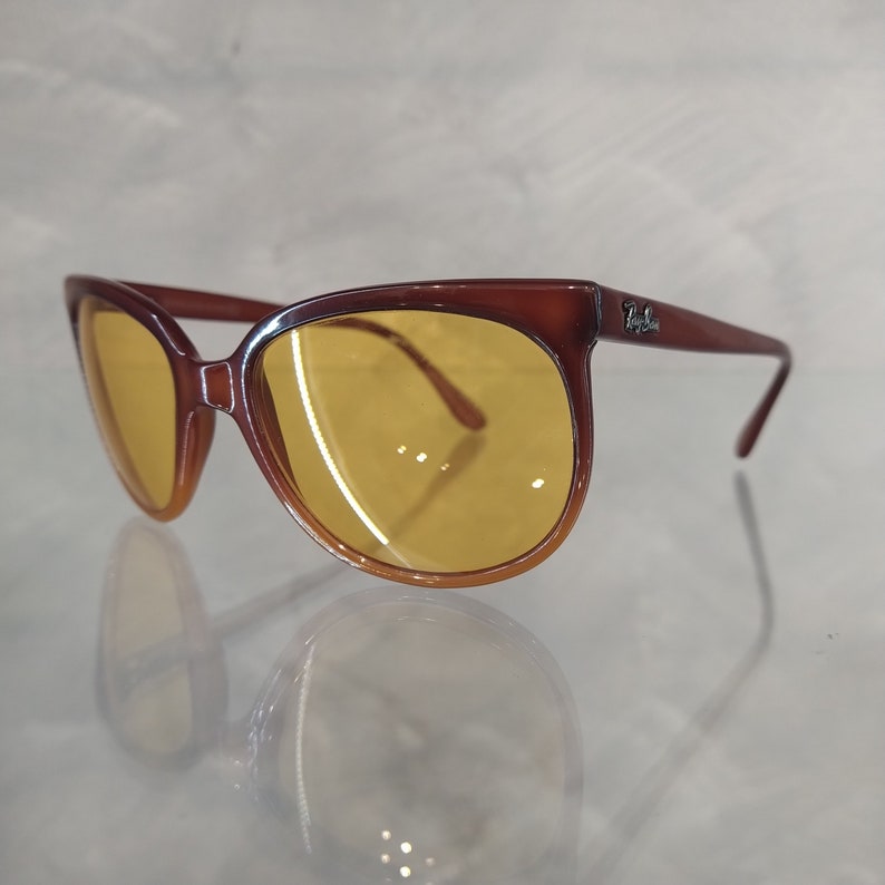 May include: Brown cat-eye sunglasses with yellow lenses and Ray-Ban branding on the side.