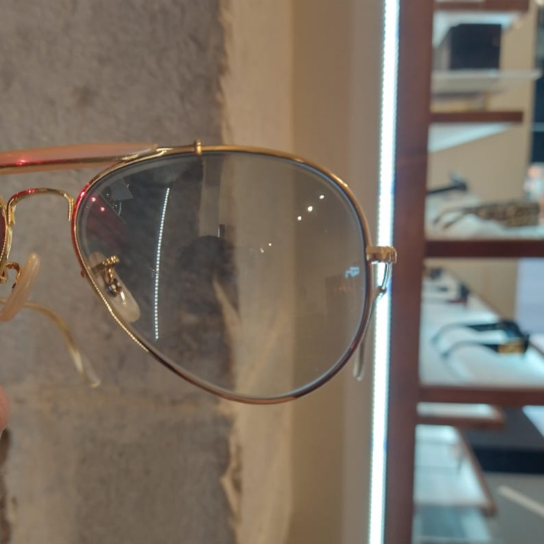 May include: Gold aviator sunglasses with clear lenses. The sunglasses are reflected in the lenses.