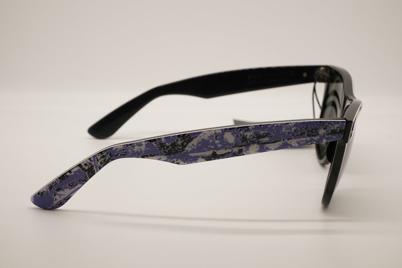 Puede incluir: Gafas de sol negras con un patr&oacute;n de camuflaje morado y gris en las patillas.