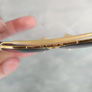 Puede incluir: Primer plano del interior de unas gafas de sol con montura dorada y lentes negras. Las gafas tienen un puente de metal dorado y el texto "W.V. 14K" est&aacute; grabado en el puente.