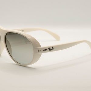 Puede incluir: Gafas de sol Ray-Ban color crema con montura redondeada y lentes degradadas. Las gafas tienen una montura y patillas gruesas, con el logotipo de Ray-Ban en el lateral. Las lentes pasan de un tono m&aacute;s oscuro a uno m&aacute;s claro.