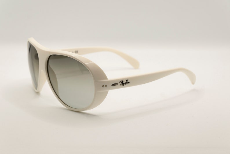 Puede incluir: Gafas de sol Ray-Ban color crema con montura redondeada y lentes degradadas. Las gafas tienen una montura y patillas gruesas, con el logotipo de Ray-Ban en el lateral. Las lentes pasan de un tono m&aacute;s oscuro a uno m&aacute;s claro.