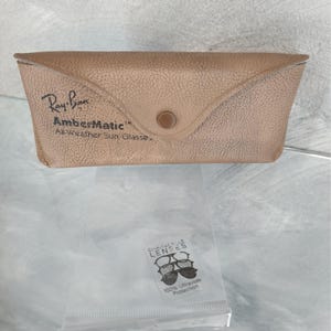 May include: Tan Ray-Ban sunglasses case with the text "Ray-Ban AmberMatic All-Weather Sun Glasses." A small plastic bag with "Chantelle Lenses" and "100% Ultraviolet Protection" is below the case.