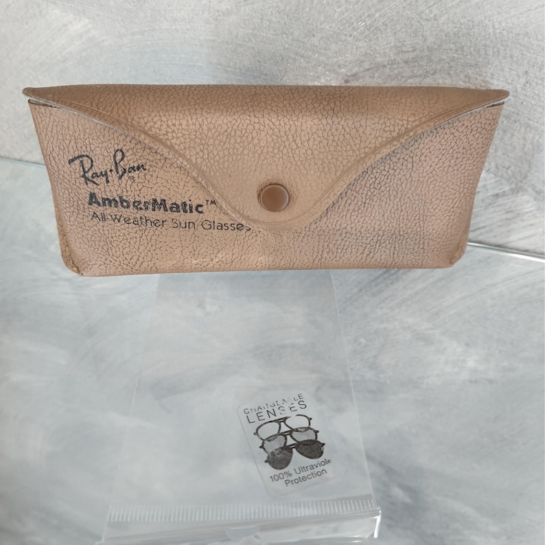 May include: Tan Ray-Ban sunglasses case with the text "Ray-Ban AmberMatic All-Weather Sun Glasses." A small plastic bag with "Chantelle Lenses" and "100% Ultraviolet Protection" is below the case.