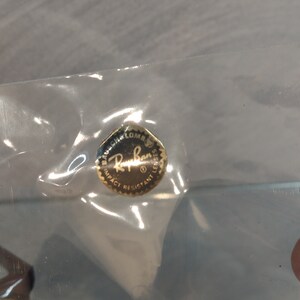 May include: A gold-colored sticker with the text "Bausch & Lomb Ray-Ban Lenses Impact Resistant" in black lettering.