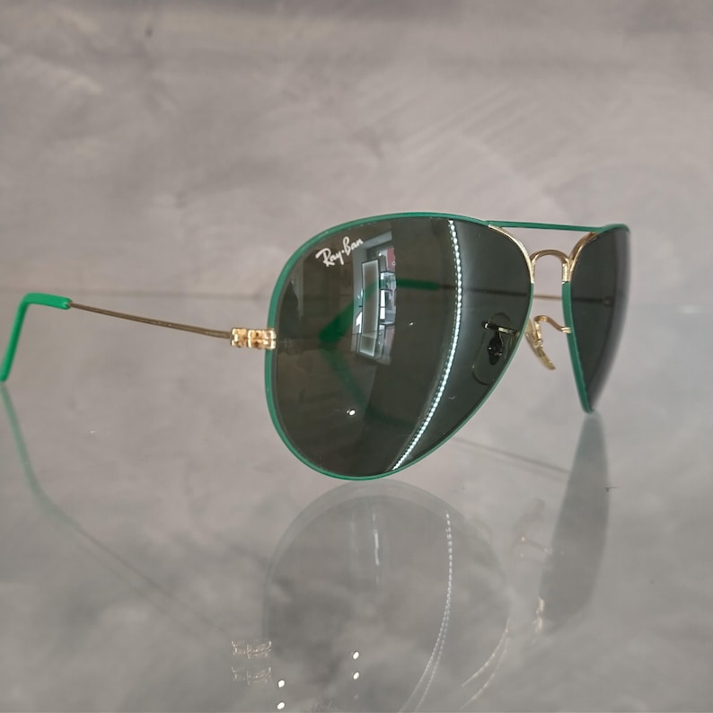 Op de afbeelding: Groene aviator zonnebril met gouden montuur en groene glazen. De zonnebril heeft het Ray-Ban logo op de linker lens.