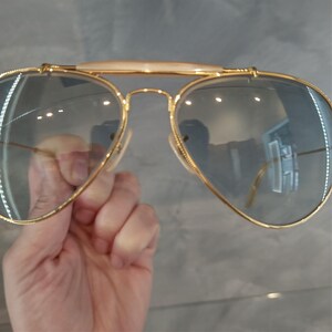 May include: Gold aviator sunglasses with a light blue lens. The sunglasses have a double bridge and a thin gold frame.