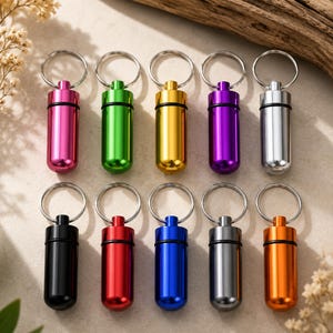 Ten colorful aluminum keychain pill containers displayed in a clean flat lay product arrangement for color variations.