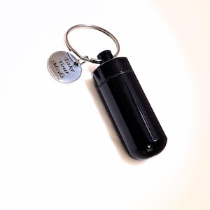 Black engraved pet medication holder keychain silver charm on a clean beige luxury background.
