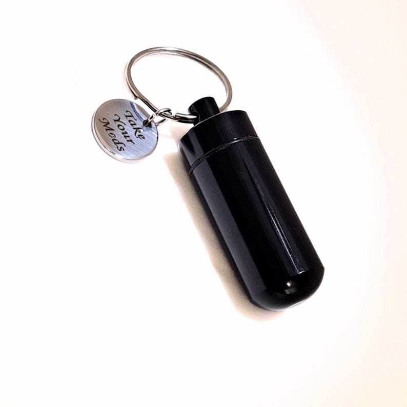Black engraved pet medication holder keychain silver charm on a clean beige luxury background.