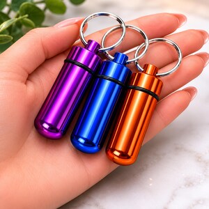 Three colorful metallic pet pill cases held in a hand to show compact travel size and portability.