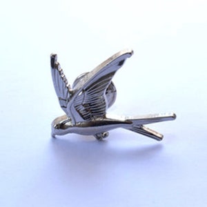 May include: Silver-toned metal bird pin with detailed wings and a long tail. The bird is in flight with its wings spread wide.