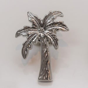 May include: A silver palm tree pin with a detailed design. The pin is a great addition to any tropical themed outfit.