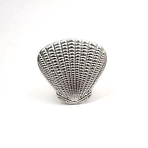 May include: A silver seashell-shaped ring holder. The holder is made of metal and has a detailed, textured surface.