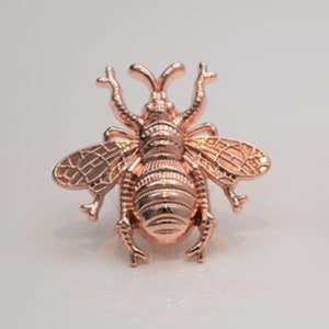 May include: A rose gold bee brooch with detailed wings and a textured body.