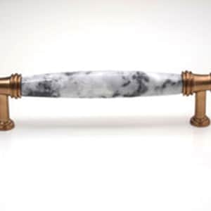 May include: A white marble cabinet pull with a bronze finish. The pull has a rectangular shape with rounded edges.