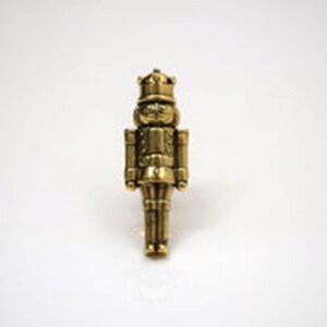 May include: A gold-coloured metal nutcracker figurine. The nutcracker is wearing a crown and has a moustache.