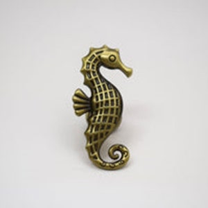 May include: A gold-toned seahorse figurine with a detailed, textured design. The seahorse is facing right and has a curled tail.