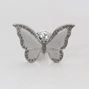 May include: A white butterfly-shaped cabinet knob with clear rhinestone accents. The knob is made of metal and has a silver finish.