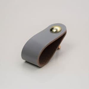 May include: A grey leather cabinet pull with a gold metal knob.