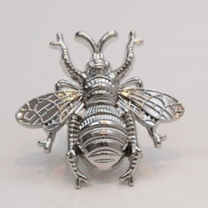 May include: A silver bee-shaped decorative object with intricate details. The bee has a textured body and wings.