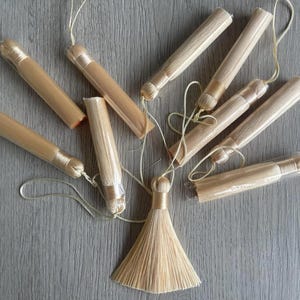 May include: A set of ten small, natural-coloured, hand-tied tassels with a long, thin, string attached to each. The tassels are arranged in a circle around a larger, natural-coloured, hand-tied tassel.