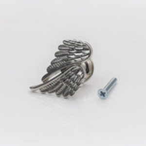 May include: A silver cabinet knob featuring a detailed wing design. A small screw is included, ready for fitting. The wing design adds a decorative element to furniture. The knob is made of metal.
