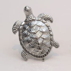 May include: A silver metal turtle figurine with a detailed shell design. The turtle is facing right and has a slightly raised head.
