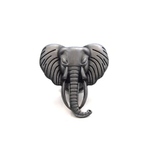 May include: A silver-coloured elephant head pin. The pin is detailed with textured lines and a raised trunk.