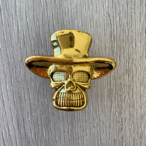 May include: Gold-toned skull wearing a top hat, a decorative accent for a home or office.
