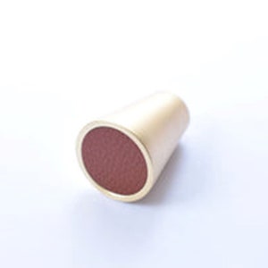 May include: A gold-coloured cone-shaped cabinet knob with a red leather top.