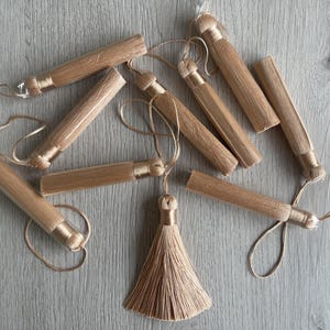 May include: A set of eight beige tassel pulls with a long, thin, and slightly twisted shape. The tassels are made of a soft, silky material and have a simple, elegant design.