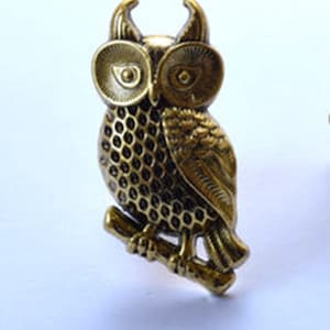 May include: A gold-toned owl figurine with detailed features, perched on a branch. The owl has large, round eyes and a textured body.
