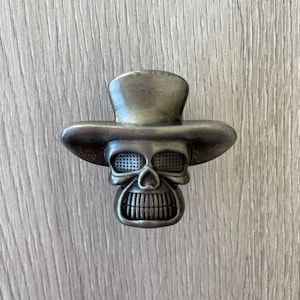 May include: A silver skull wearing a top hat, a decorative cabinet knob.