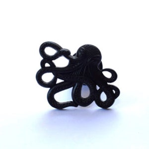 May include: Black octopus shaped cabinet knob or drawer pull. The octopus has a detailed design with tentacles.