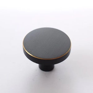 May include: A round black cabinet knob with a gold trim. The knob has a small, round base.