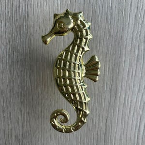 May include: Gold-toned metal seahorse door knob with a textured surface.