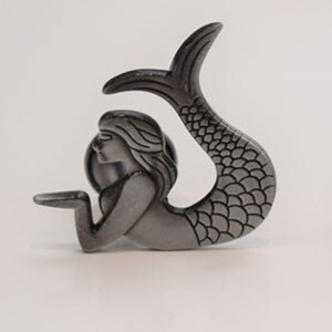 May include: A silver-toned mermaid figurine with a detailed tail and flowing hair. The mermaid is holding a small, round object in her hand.