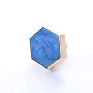 May include: A hexagonal ring with a blue stone set in a gold setting.